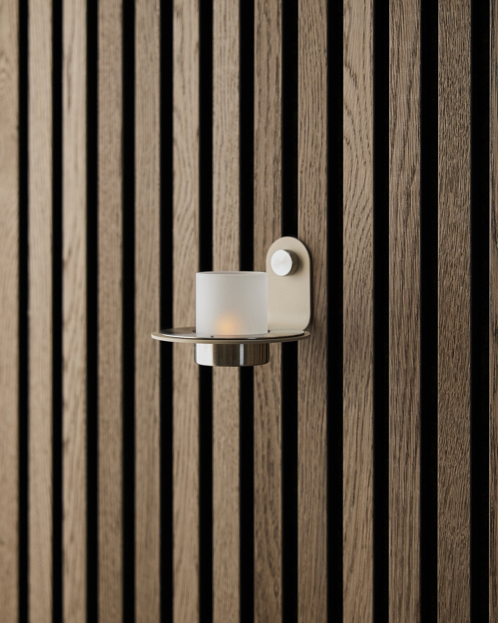 Der Norr Kerzenhalter in beige Edelstahl von WoodUpp, präsentiert an einer Wand aus beige Akupanel Akustikpaneel.